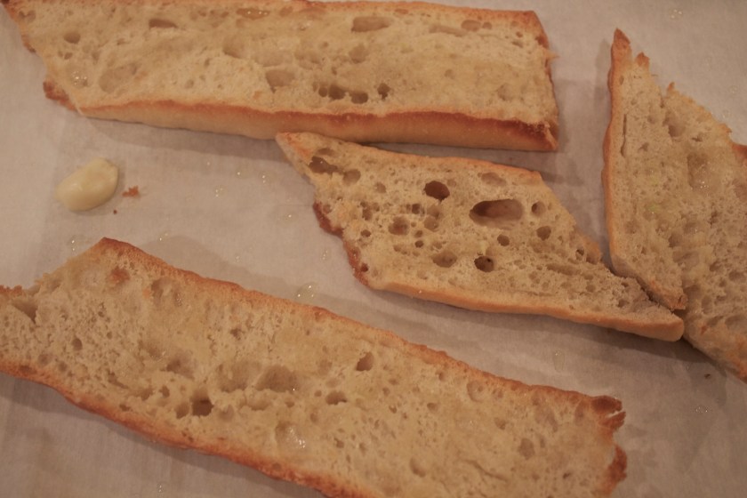 Cut baguette in half, then into diagonal sections, and sprinkle olive oil on top. Into a 400 degree oven for 10 minutes.